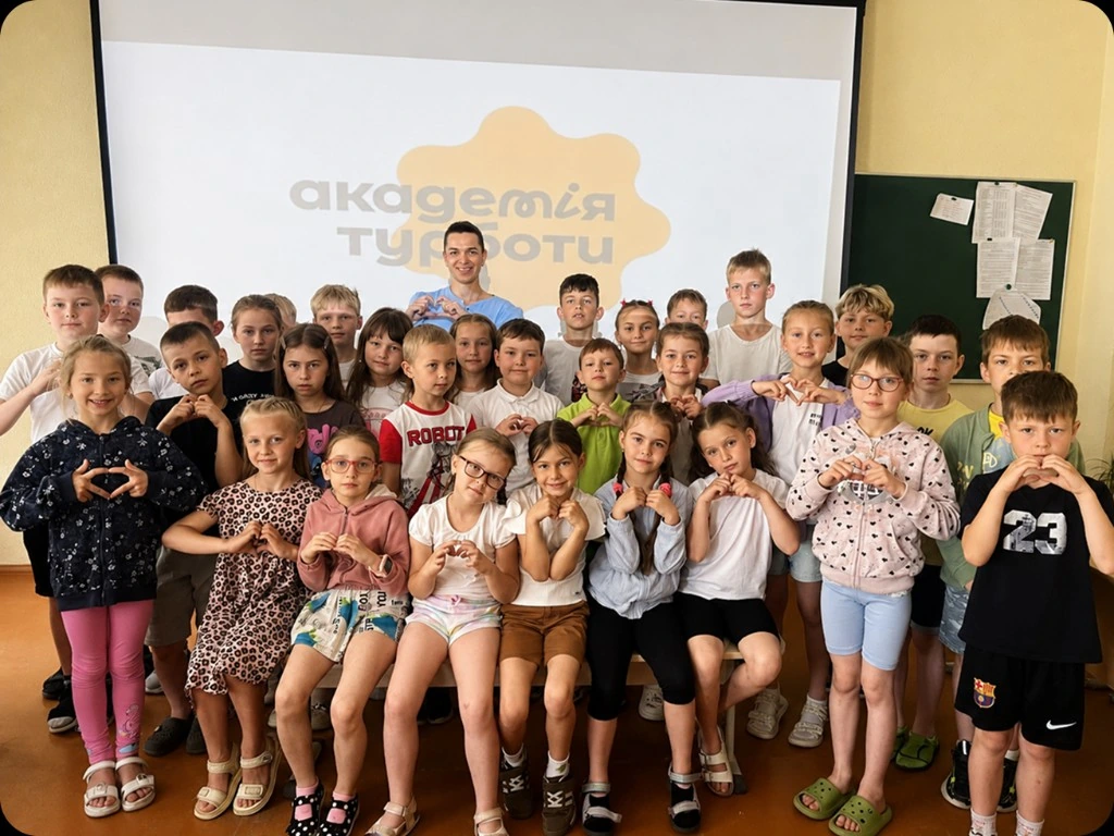 Діти складають серця руками біля екрана Академії Турботи